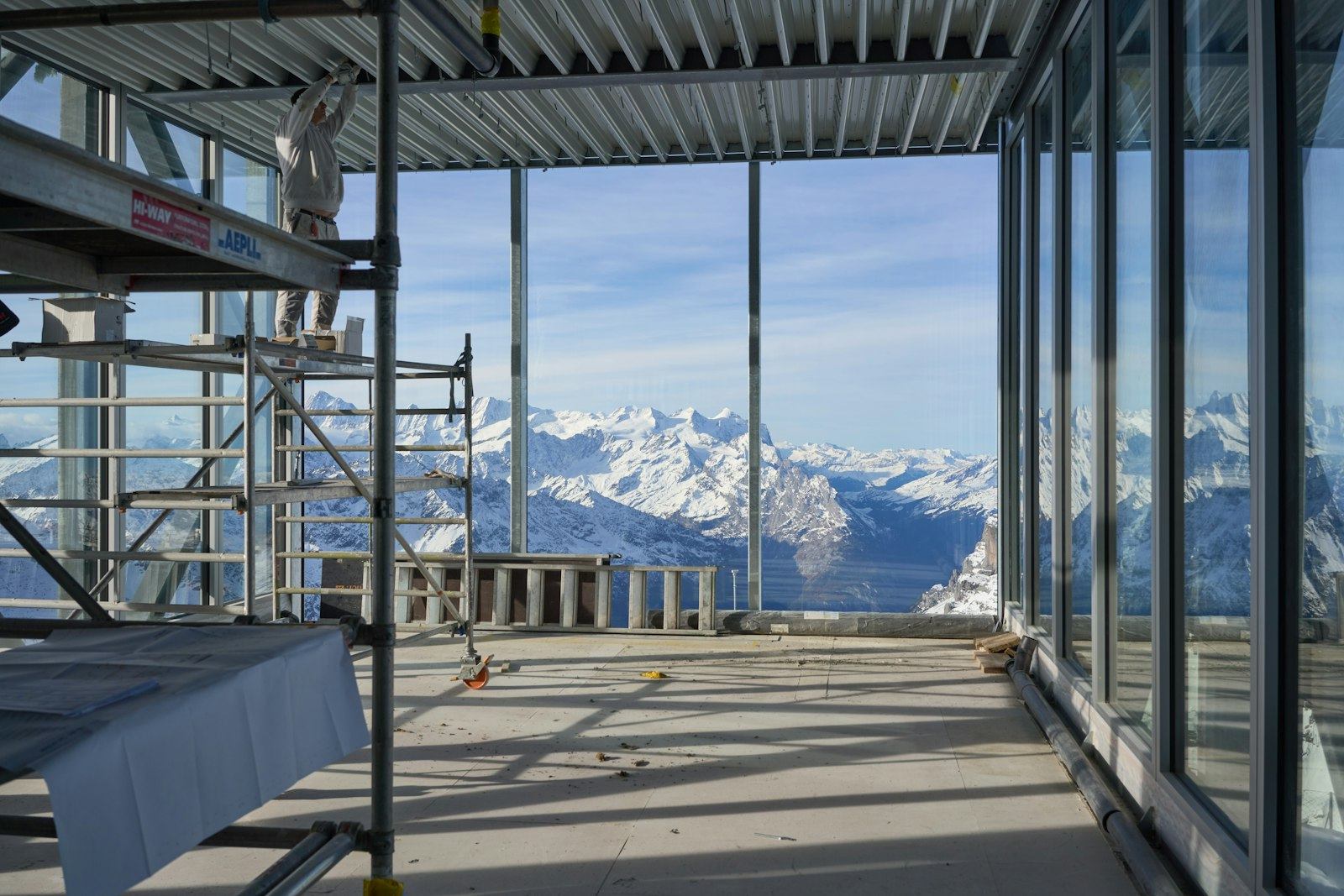 Chantier en cours face aux sommets enneigés des Alpes, échafaudage et grandes baies vitrées